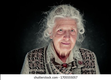 Elderly Gray-haired Woman Dressed In A White Blouse With Embroidery And An Amber Vintage Brooch. She Looks Like A Professor, Doctor Or Scientist Dignity, Confidence, Wisdom. 