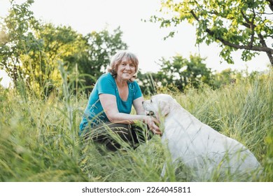 Elderly grayhaired woman with her lovely dog in the park. Portrait of a smiling senior female sitting outside with her golden labrador on grass. Happy aged woman hugging her pet. - Powered by Shutterstock