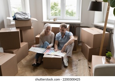 Elderly Grey Haired Couple Choosing Colors For New Home Interior, Reviewing Paper Brochure With Samples, Pointing At Different Swatches, Planning Renovation After Moving Into New Apartment