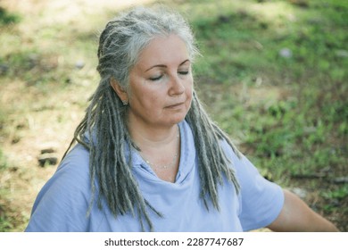 Elderly grey haired woman with dreadlocks in her 60s sitting closed eyes outdoors - meditation and daydreaming concept - Powered by Shutterstock