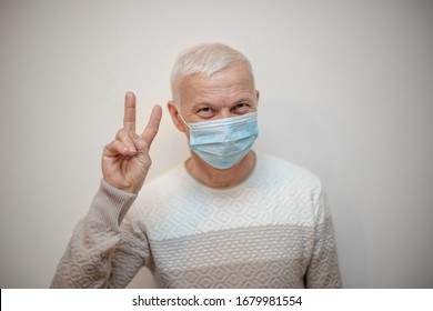 elderly handsome man in medical mask raised up two fingers, shows sign victory.. pensioner in protective mask advises to protect against viruses, coronavirus, influenza