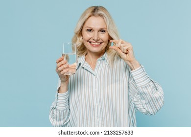 Elderly Happy Woman 50s Wear Casual Striped Shirt Hold Glass Of Water Medication Tablets, Aspirin Pills Isolated On Plain Pastel Light Blue Color Background Studio Portrait. People Lifestyle Concept