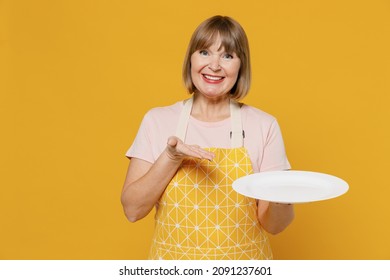 Elderly housekeeper housewife woman 50s in orange apron point hand on empty plate with copy space workspace area isolated plain on yellow background studio portrait. People household lifestyle concept - Powered by Shutterstock