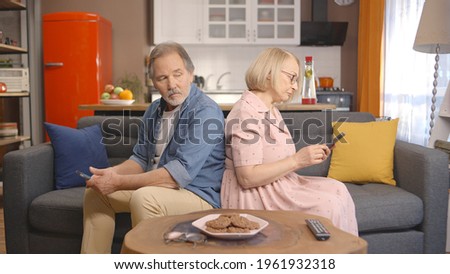 The elderly husband and wife, who are angry with each other, are sitting on  their back to back and hanging around with their phones while they wonder what the other is doing on the phone. 