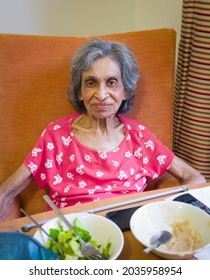 Elderly Indian Woman In A Care Home Or Nursing Home, UK, Sitting In A Chair Eating A Meal. Depicts Frailty And Malnutrition In Old Age