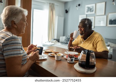 Elderly interracial couple eating breakfast together at kitchen table - Powered by Shutterstock