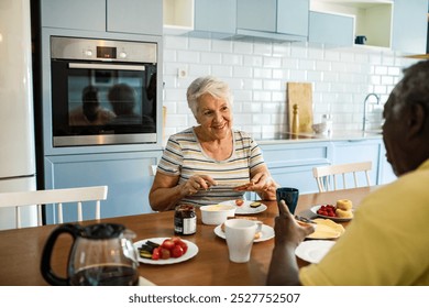 Elderly interracial couple eating breakfast together at kitchen table - Powered by Shutterstock