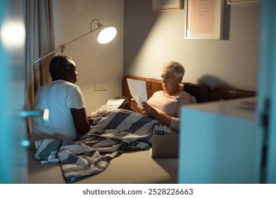 Elderly interracial couple managing finances in bed with laptop - Powered by Shutterstock