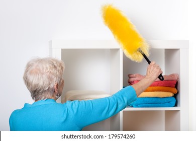 Elderly Lady During Dusting Furniture At Home