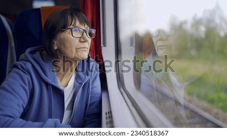 Elderly lady in glasses travels in train and looking out the window reflected in the glass