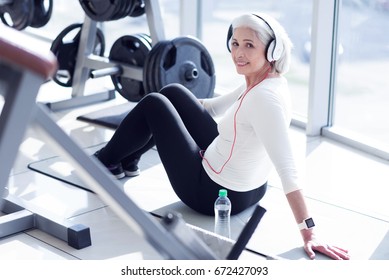 Elderly lady with headphones sitting at gym