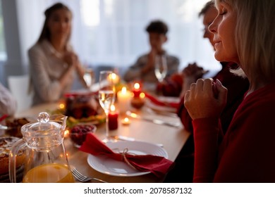 Elderly lady and her extended family praying, expressing thanks to God, sitting at table with festive meal at home, copy space. Senior woman with her nears celebrating Christmas or Thanksgiving - Powered by Shutterstock