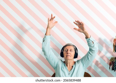 Elderly Lady In Her Seventies Listens To Music With Headphones Moving Her Arms In The Air And Letting Herself Be Carried Away By The Sound Keeping Her Eyes Closed - Leisure Time