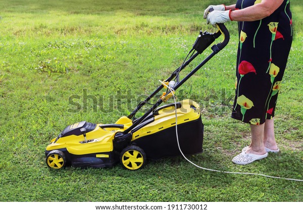 Elderly lady pushing an electric mower to cut the\
grass. Active seniors are passionate about their hobbies and lead\
meaningful quiet lives