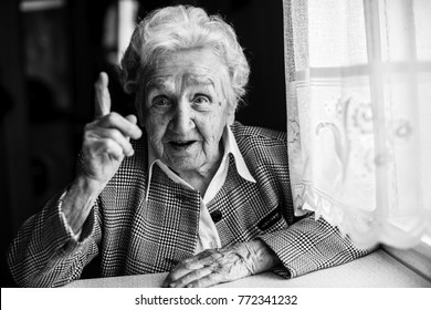 Elderly Lady Speaks Sitting At The Table. Black And White Portrait.