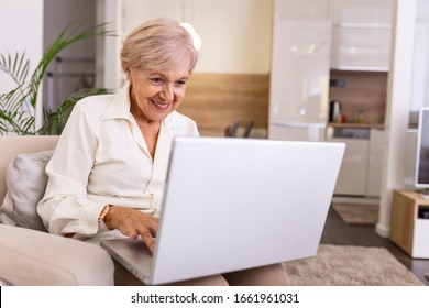 Elderly Lady Working With Laptop. Portrait Of Beautiful Older Woman Working Laptop Computer Indoors. Senior Woman Using Laptop At Home, Laughing