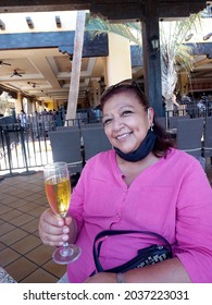 Elderly Latina Woman Drinking A Glass Of Wine With A Mask In The New Normal Due To The Covid-19 Pandemic
