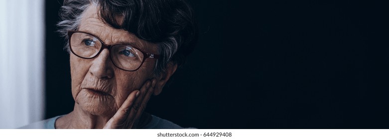 Elderly lonely woman with Alzheimer's sadly looking through the window