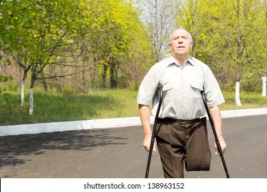 Elderly Male Amputee Balanced On Crutches In A Rural Street With His Trousers Pinned Up To Reveal His Stump