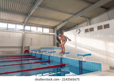 An elderly male athlete in a hat and glasses jumps from a height into the pool