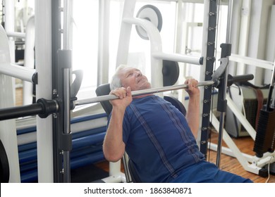 Elderly male is having intense workout in gym. Senior caucasian man lifting weights at fitness club. Strength workout for seniors. - Powered by Shutterstock