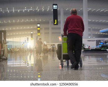 An elderly male passenger is trolling his airport bag to the check-in counter for airline travel. The airport is very modern and very large. Concept traveling by airplane is easy and very popular.