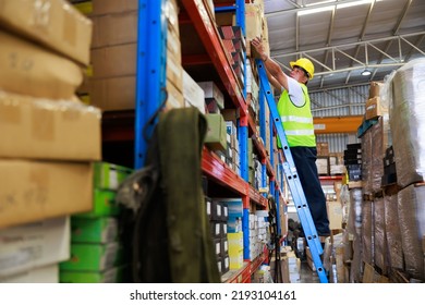 elderly male warehouse worker climbs the stairs to lift the cardboard boxes on the shelf. Yellow Safety hard hat helmet.  - Powered by Shutterstock