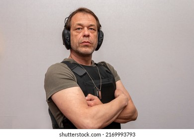 An Elderly Man 45-50 Years Old In A Bulletproof Vest And Tactical Headphones For Shooting On A Light Background.