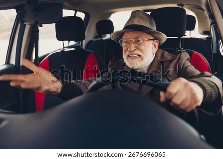 Elderly man animatedly gestures while driving car, showcasing emotion and energy inside modern vehicle