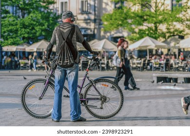 An elderly man with a backpack and headphones standing with his bicycle in a busy city square. City life, transport or leisure concept illustration - Powered by Shutterstock