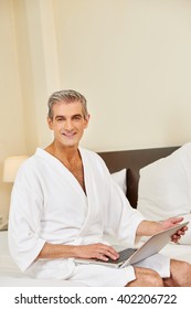 Elderly Man In Bathrobe With Laptop Computer In A Hotel Room