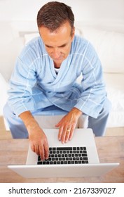 An Elderly Man In Bathrobe Working On A Laptop At Home. Upward View Of A Senior Retired Man Working On A Laptop At Home.