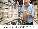 Elderly man carefully reading product labels in the dairy aisle, mindful of health choices