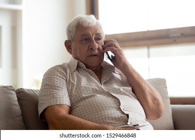 Elderly man in casual clothes seated on couch in living room holding mobile phone talking having distant communication with doctor getting services or recommendations from therapist counsellor concept - Powered by Shutterstock