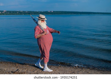 An Elderly Man In A Classic Bathing Suit Walks Along The Beach With An Umbrella On A Hot Summer Day