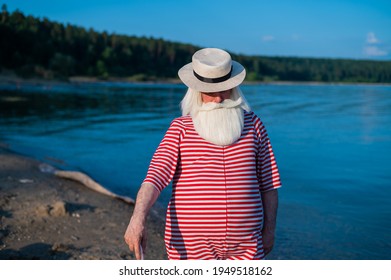 An Elderly Man In A Classic Bathing Suit Walks Along The Beach With An Umbrella On A Hot Summer Day