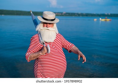 An Elderly Man In A Classic Bathing Suit Walks Along The Beach With An Umbrella On A Hot Summer Day