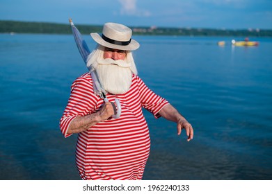 An Elderly Man In A Classic Bathing Suit Walks Along The Beach With An Umbrella On A Hot Summer Day