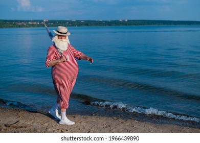 An Elderly Man In A Classic Bathing Suit Walks Along The Beach With An Umbrella On A Hot Summer Day