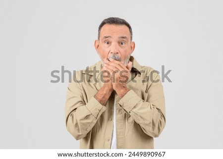 An elderly man covers his mouth in shock, displaying a surprised expression, isolated on a white background