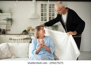 An Elderly Man Covers His Wife With A Warm Blanket To Keep Warm In Winter.