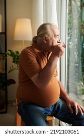 Elderly Man Drinking Cup Of Tea And Looking Outside Through Glass Doors