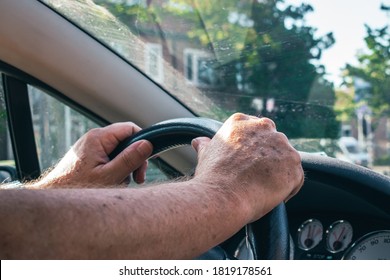 Elderly man driving with both hands on the steering wheel in a cabrio peugeot car in the city 