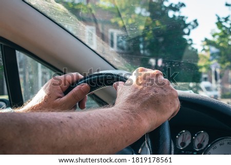 Elderly man driving with both hands on the steering wheel in a cabrio peugeot car in the city 