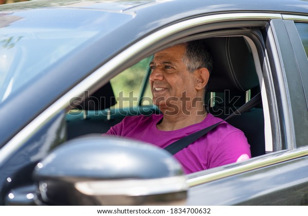 Elderly man\
driving car. A middle eastern dark skin senior retired man driving\
a car, portrait from the\
side.