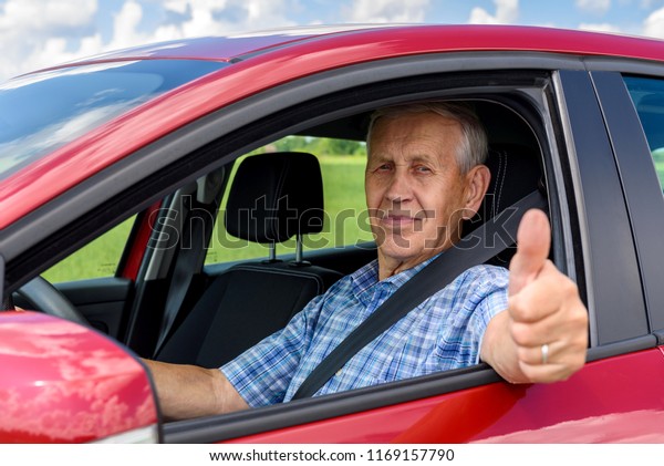 elderly man\
driving the car and shows the\
thumb
