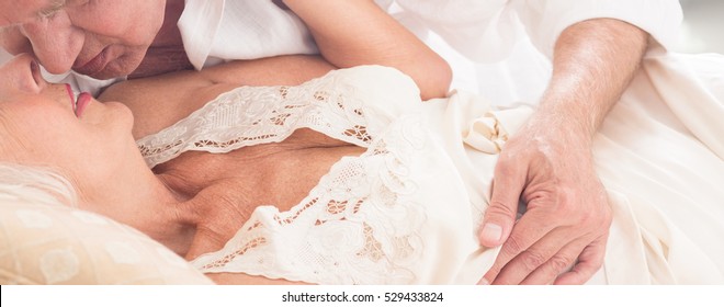 Elderly Man Embracing And Kissing His Lovely Older Wife In Sexy Lingerie Lying In Bed