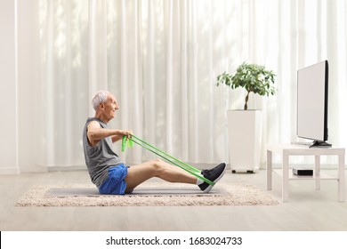 Elderly Man Exercising With An Elastic Band In Front Of A Tv At Home