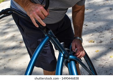 elderly man fixing his blue bike from the chest down wearing gray t shirt dark gray shorts and a watch cement background - Powered by Shutterstock