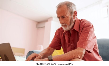 Elderly man focused on using a laptop in a cozy home setting, showcasing technology use among older adults in a casual environment